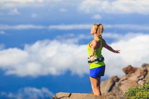 Happy woman runner joyful with arms raised outstretched smiling and ecstatic happiness with eyes closed. Fitness and exercise meditation in summer mountains nature outdoors, freedom concept.