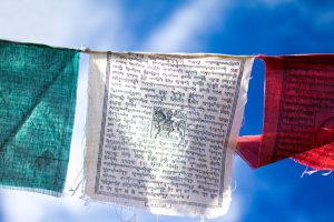 Colorful (green, white, red) Tibetan Buddhist prayer flags fluttering against a cloudy blue sky (close-up).